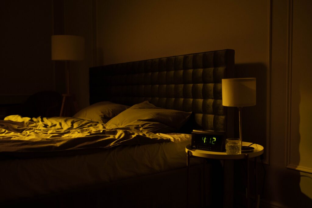 Camera da letto in penombra con letto disfatto e una sveglia digitale che segna le 04:12.